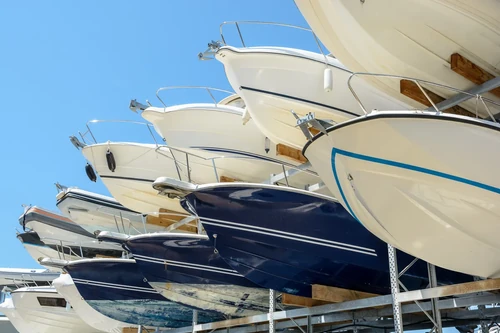 View from below of motorboats stored on multi-level racks at a boat storage yard against a clear blue sky.