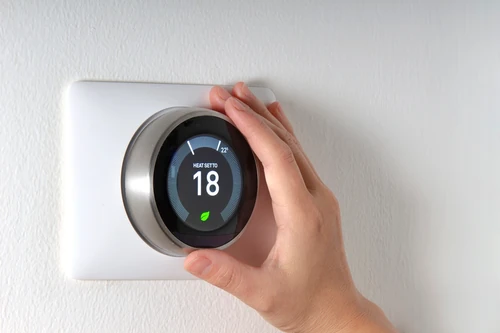 Hand adjusting a smart thermostat displaying temperature settings on a wall-mounted control panel.
