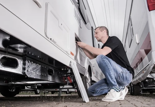 Man inspecting RV exterior as part of routine maintenance.