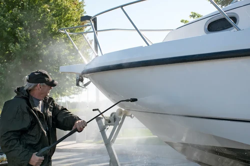 Man cleaning boat with pressure washer on trailer outdoors. 