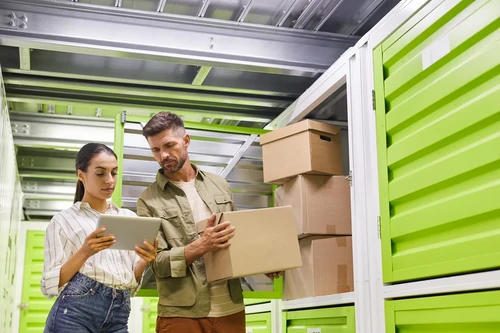 ouple organizing cardboard boxes inside a storage unit while checking items on a tablet.
