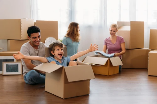 Family unpacking boxes in a living room with child sitting inside a cardboard box.