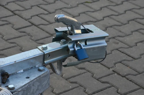 Padlock securing trailer hitch on metal coupling over paved ground. 