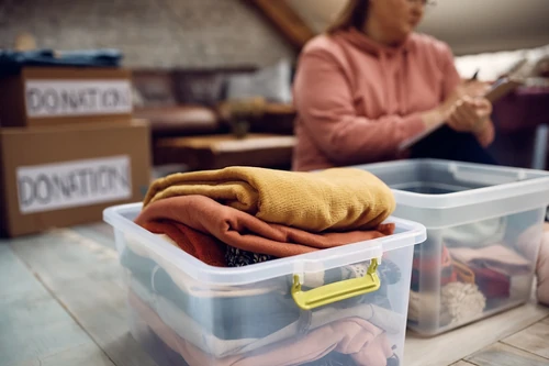 Clothes folded in reusable storage bins with donation boxes in background, showing eco-friendly organization.