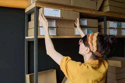 Woman placing labeled boxes on shelves inside a storage unit.