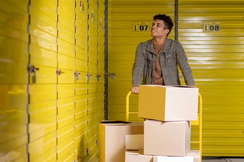 Person moving boxes on a hand truck down a hallway of storage units.