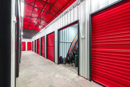 Indoor climate controlled storage units with red roll up doors, bright lighting, and visible stored items in one unit.