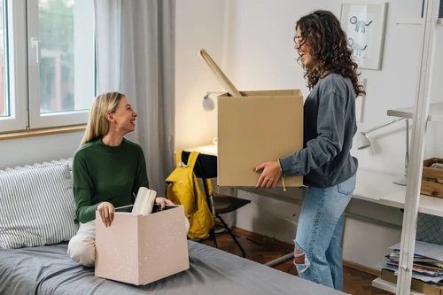 Two female students packing boxes in a dorm room, organizing belongings for storage preparation.