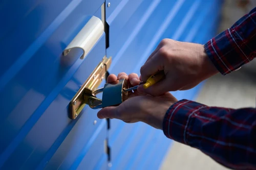 Person unlocking a storage unit door with a key, showing a close-up of a lock and handle on a metal roll-up door.