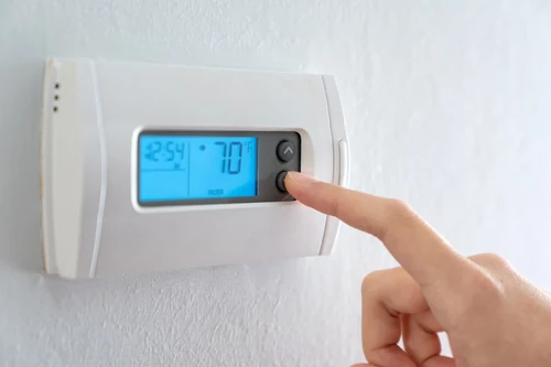 Hand adjusting a digital thermostat showing temperature control on a wall.