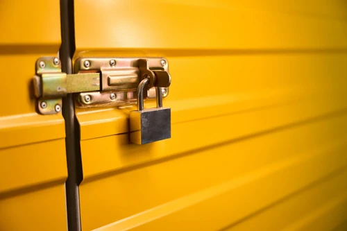 Close-up of metal latch and padlock on yellow storage unit door.
