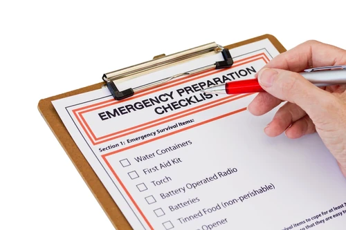 Hand holding a red pen over an emergency checklist on a clipboard.