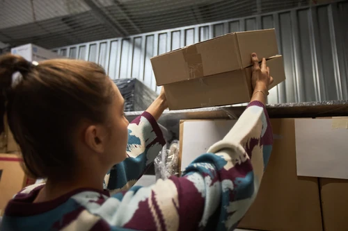 Woman placing cardboard boxes on a high shelf in a storage unit.