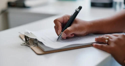 Person signing document on clipboard with pen.