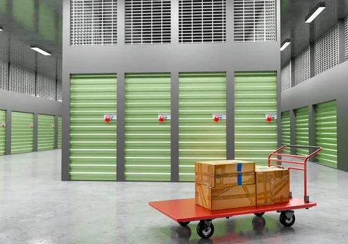 Moving cart with stacked boxes in hallway of storage facility with green unit doors.