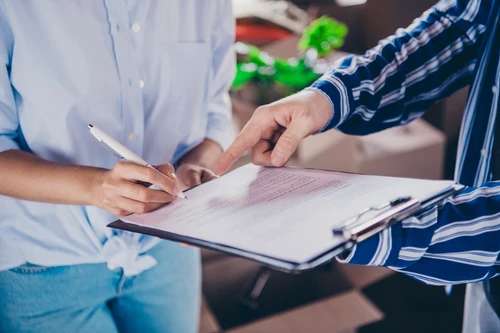 Alt text: Person signing document on clipboard while another person points at contract.