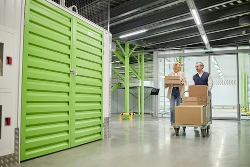 Couple pushing cart with boxes inside a storage facility hallway.