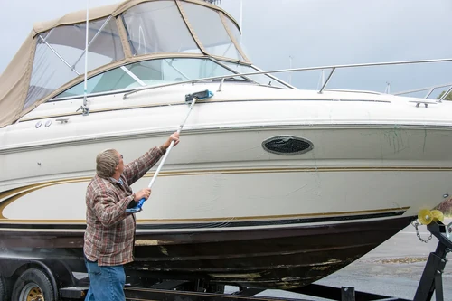 Man scrubbing side of boat with long brush on trailer. 