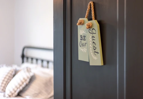 Open door of a guest bedroom with a sign that reads “be our guest.”
